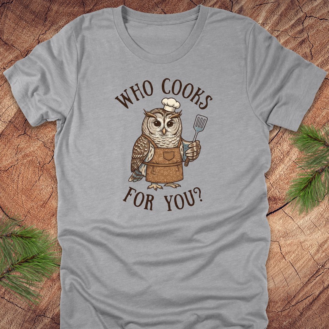Gray t-shirt with an owl graphic and text 'who cooks for you' on a wooden surface