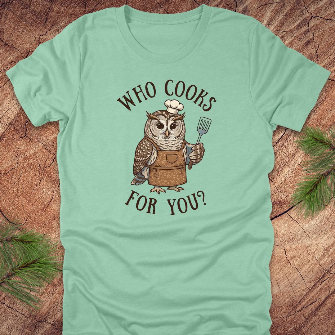 Mint green t-shirt with an owl graphic and text 'who cooks for you' on a wooden surface