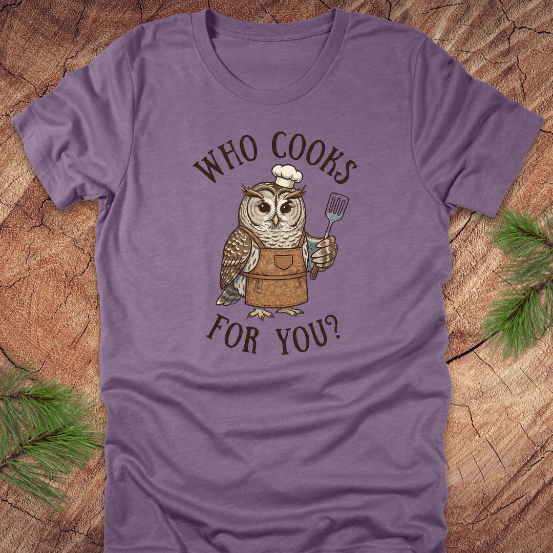 Heather purple t-shirt with an owl graphic and text 'who cooks for you' on a wooden surface