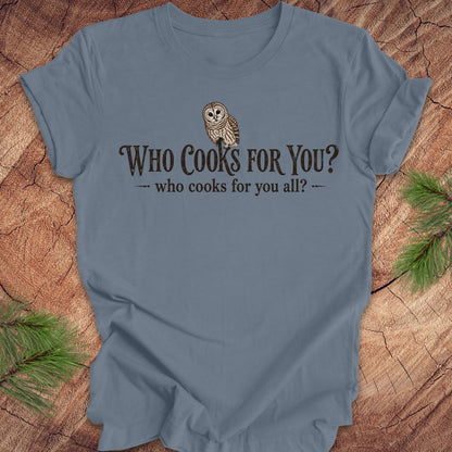 Blue t-shirt with an owl and text, 'who cooks for you?' on a wood background.