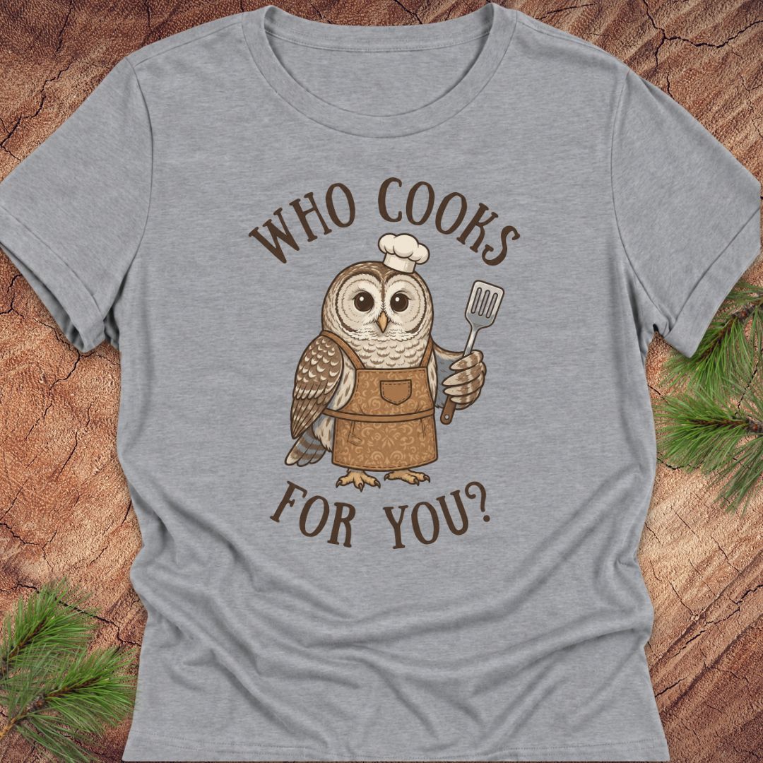 A heather gray short-sleeve t-shirt with a graphic of a cute owl wearing a chef's hat and apron, holding a spatula. The text 'WHO COOKS FOR YOU?' is printed in brown around the owl.