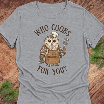 A heather gray short-sleeve t-shirt with a graphic of a cute owl wearing a chef's hat and apron, holding a spatula. The text 'WHO COOKS FOR YOU?' is printed in brown around the owl.