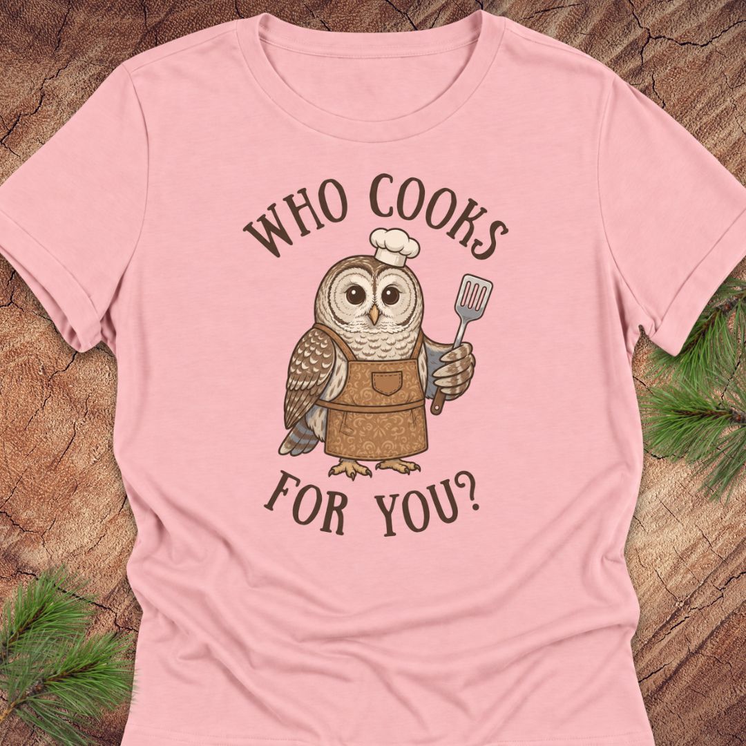 A light pink short-sleeve t-shirt with a graphic of a cartoon owl wearing a chef's hat and apron, holding a spatula. The text 'WHO COOKS FOR YOU?' is printed in brown around the owl.