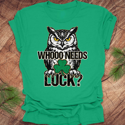 Green t-shirt with an owl st patrick's day graphic and text 'WHOO NEEDS LUCK?' on a wooden surface.