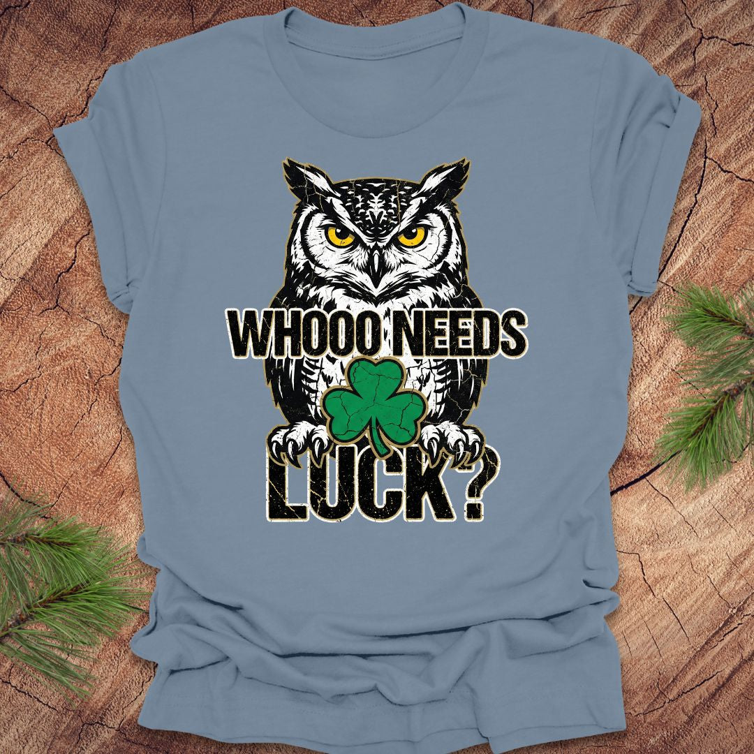 Blue t-shirt with an owl st patrick's day graphic and text 'WHOO NEEDS LUCK?' on a wooden surface.