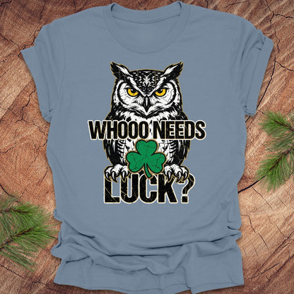 Blue t-shirt with an owl st patrick's day graphic and text 'WHOO NEEDS LUCK?' on a wooden surface.