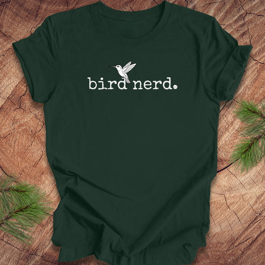 Green t-shirt with 'bird nerd' text and bird graphic on a wooden surface with pine branches.