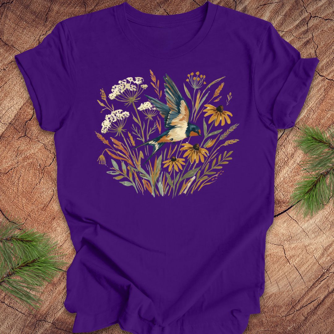 Purple t-shirt with watercolor flowers and a barn swallow in flight, on a wood background. 