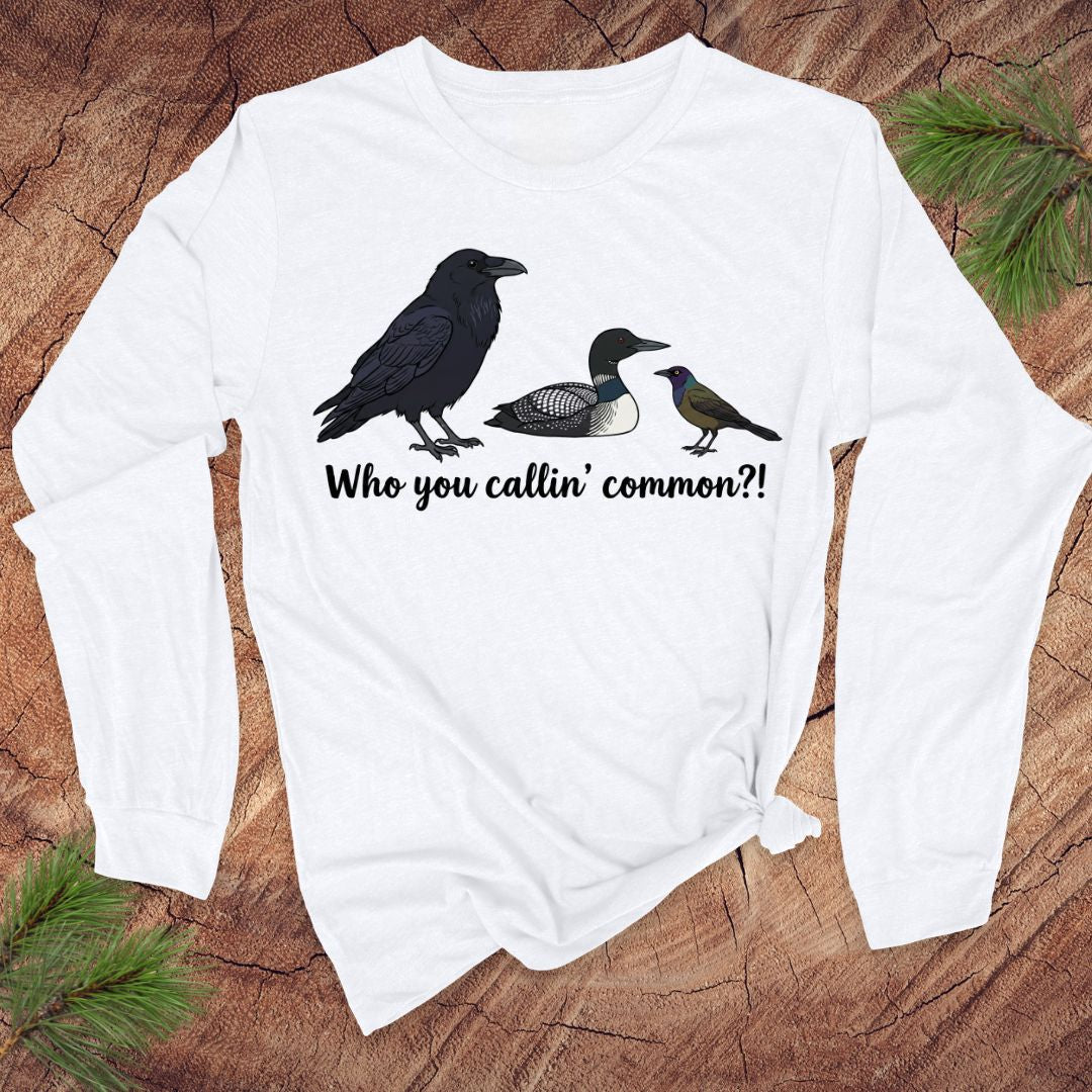 White long-sleeve shirt with bird illustrations and text on a wooden surface