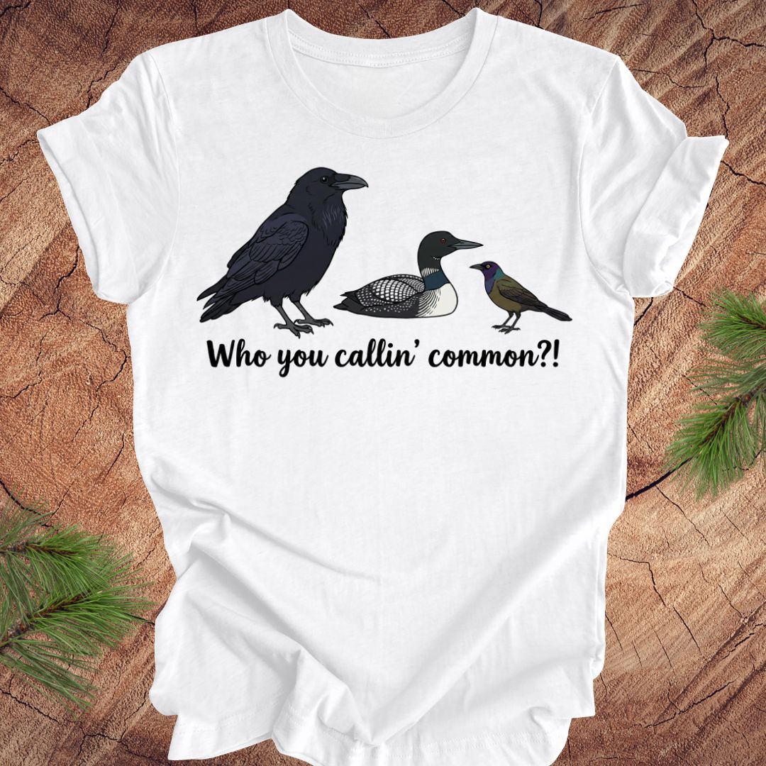 White t-shirt with bird illustrations and text on a wooden surface