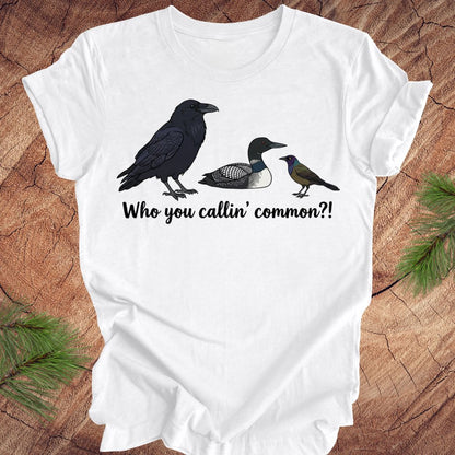 White t-shirt with bird illustrations and text on a wooden surface