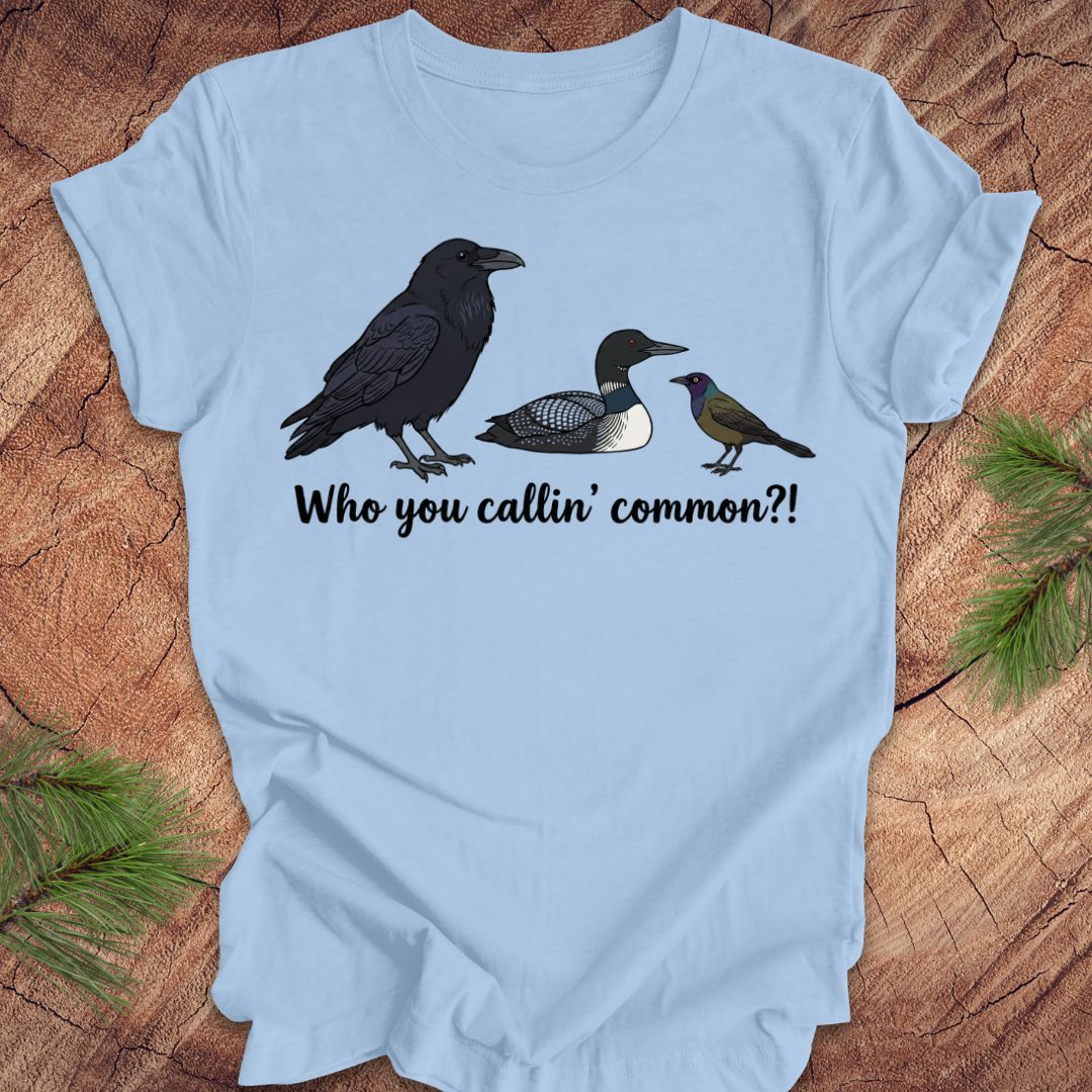 Light blue t-shirt with bird illustrations and text on a wooden surface