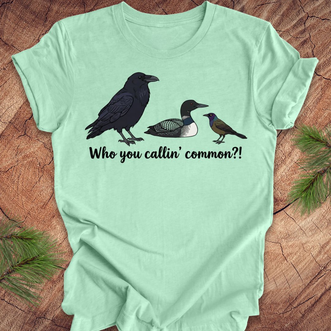 Light green t-shirt with bird illustrations and text on a wooden surface