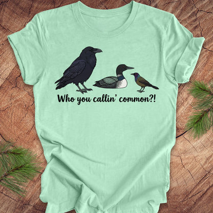 Light green t-shirt with bird illustrations and text on a wooden surface