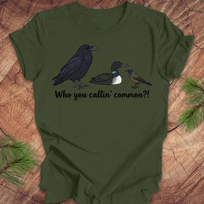 Green t-shirt with bird illustrations and text on a wooden surface