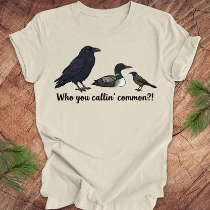 Beige t-shirt with bird illustrations and text on a wooden surface