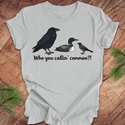 Gray t-shirt with bird illustrations and text on a wooden surface