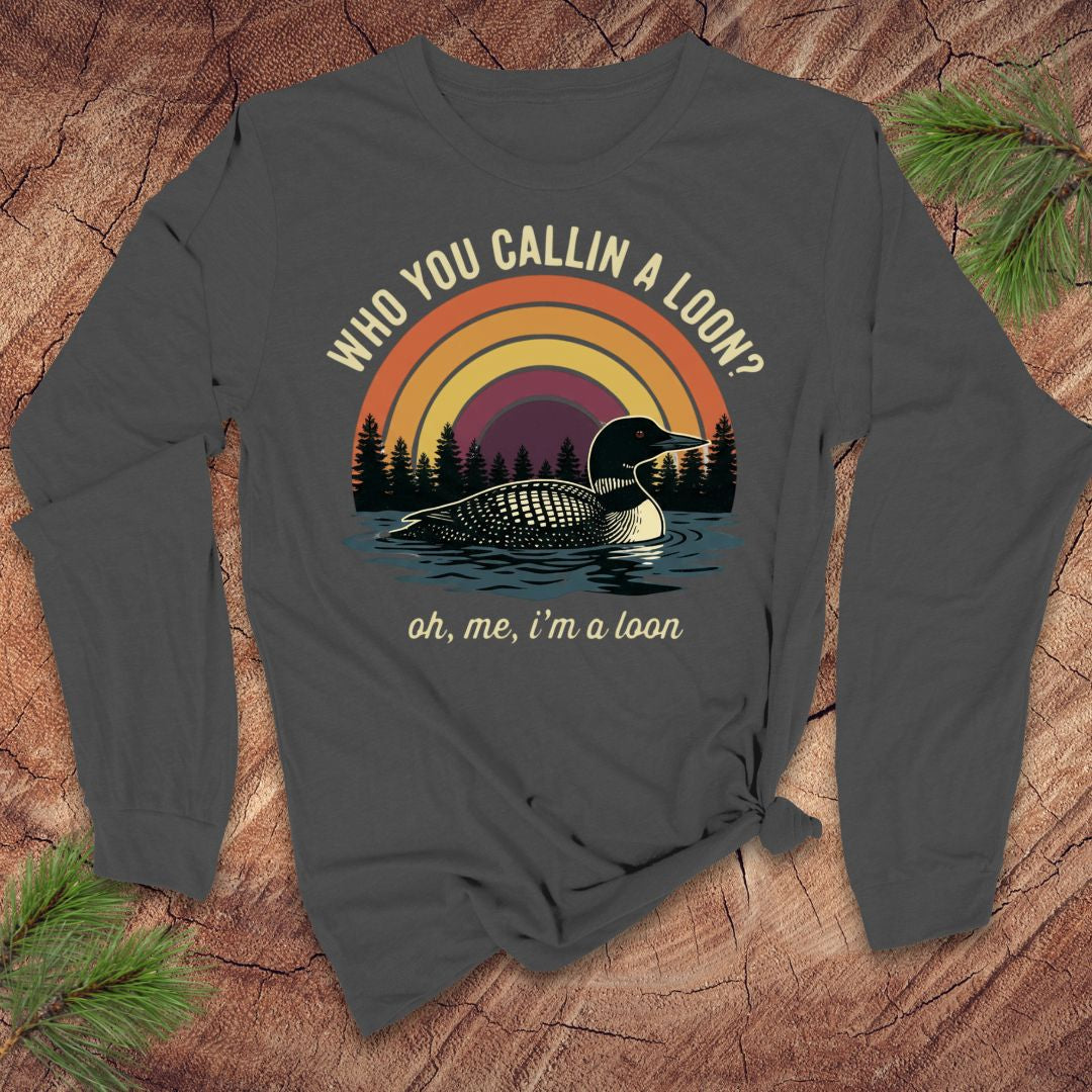 Gray long-sleeve shirt with a loon graphic and text on a wooden surface with pine branches.