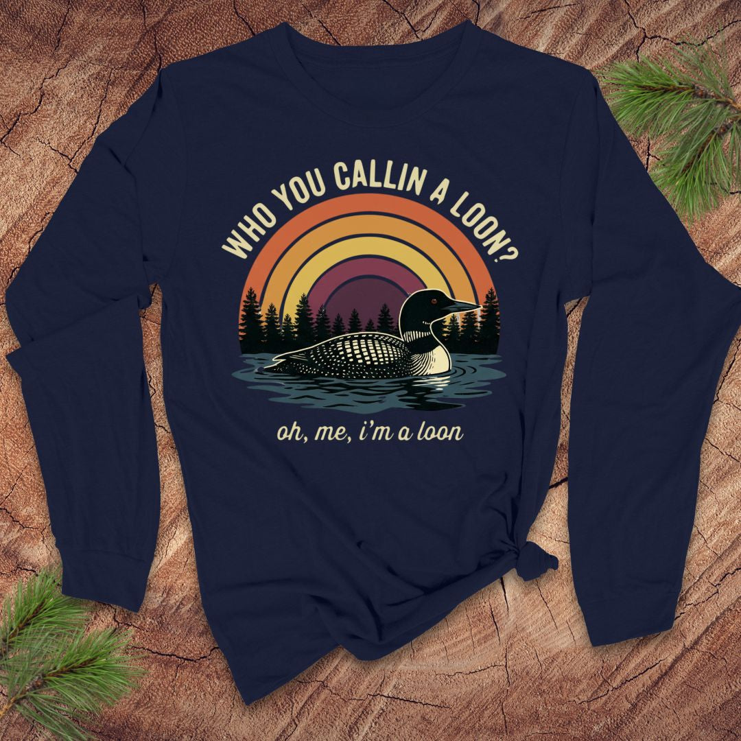 Navy blue long-sleeve tshirt with a loon graphic and text on a wooden surface with pine branches.