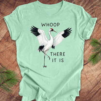 Mint green t-shirt with a crane graphic and text, 'whoop there it is' on a wooden surface