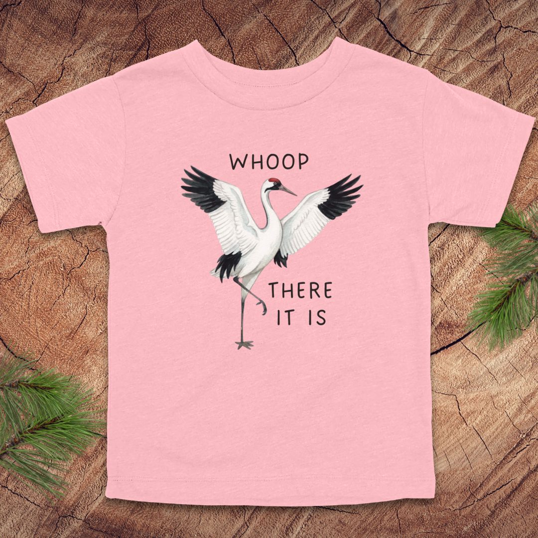 Pink t-shirt with a crane graphic and text on a wooden surface