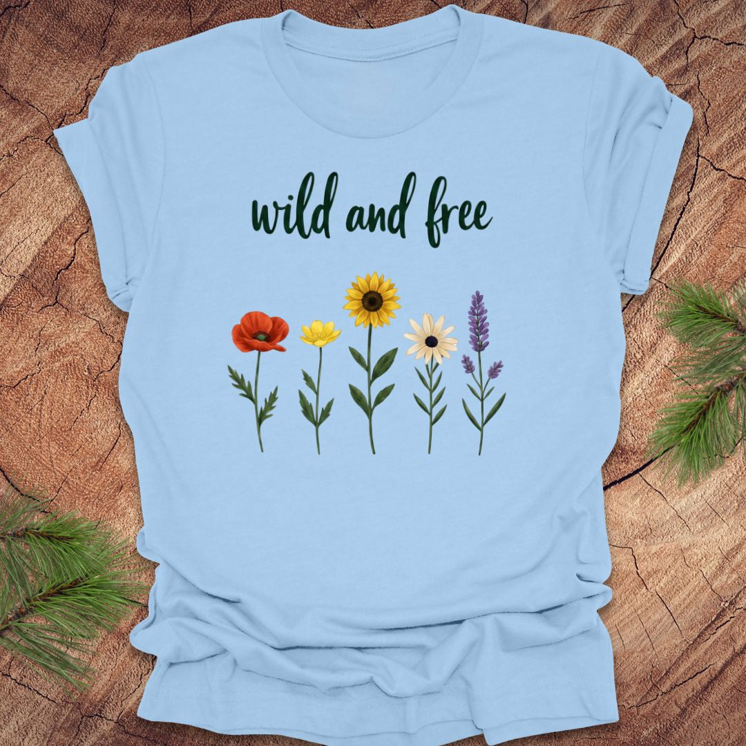Light blue t-shirt with floral designs and 'wild and free' text on a wooden surface.
