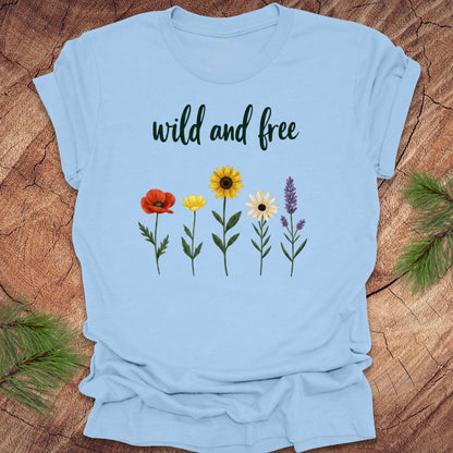 Light blue t-shirt with floral designs and 'wild and free' text on a wooden surface.