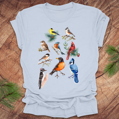 Light blue t-shirt with colorful bird illustrations on a wooden surface