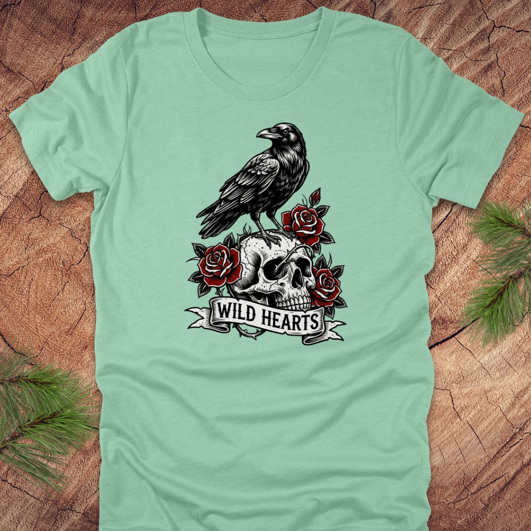 Mint green t-shirt with a crow, skull, and roses design with text, 'wild hearts' on a wooden surface.