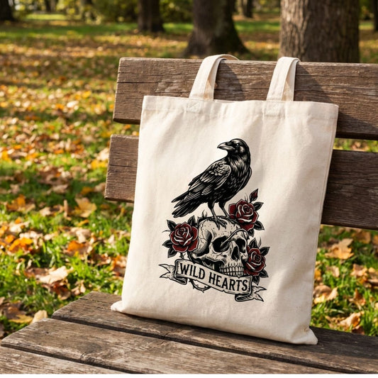 Tote bag with a raven and skull design on a wooden bench in a park.