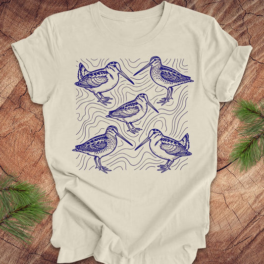 Beige t-shirt with blue woodcock and wilson's snipe bird illustrations on a wooden surface