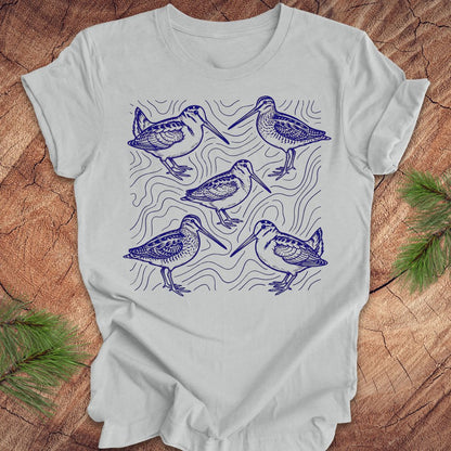 Silver t-shirt with blue woodcock and wilson's snipe bird illustrations on a wooden surface