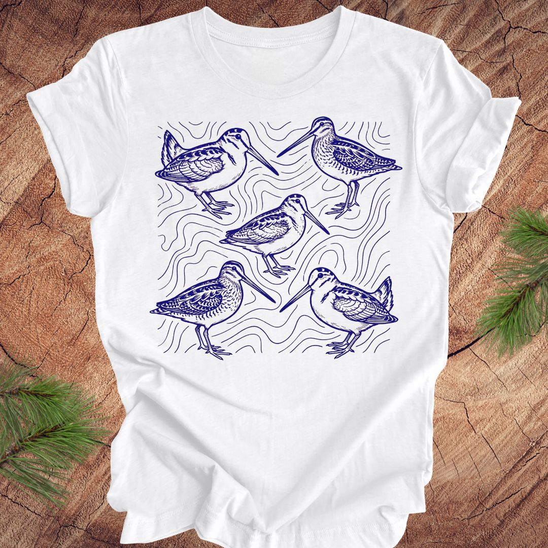 White t-shirt with blue woodcock and wilson's snipe bird illustrations on a wooden surface