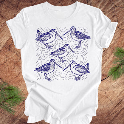 White t-shirt with blue woodcock and wilson's snipe bird illustrations on a wooden surface