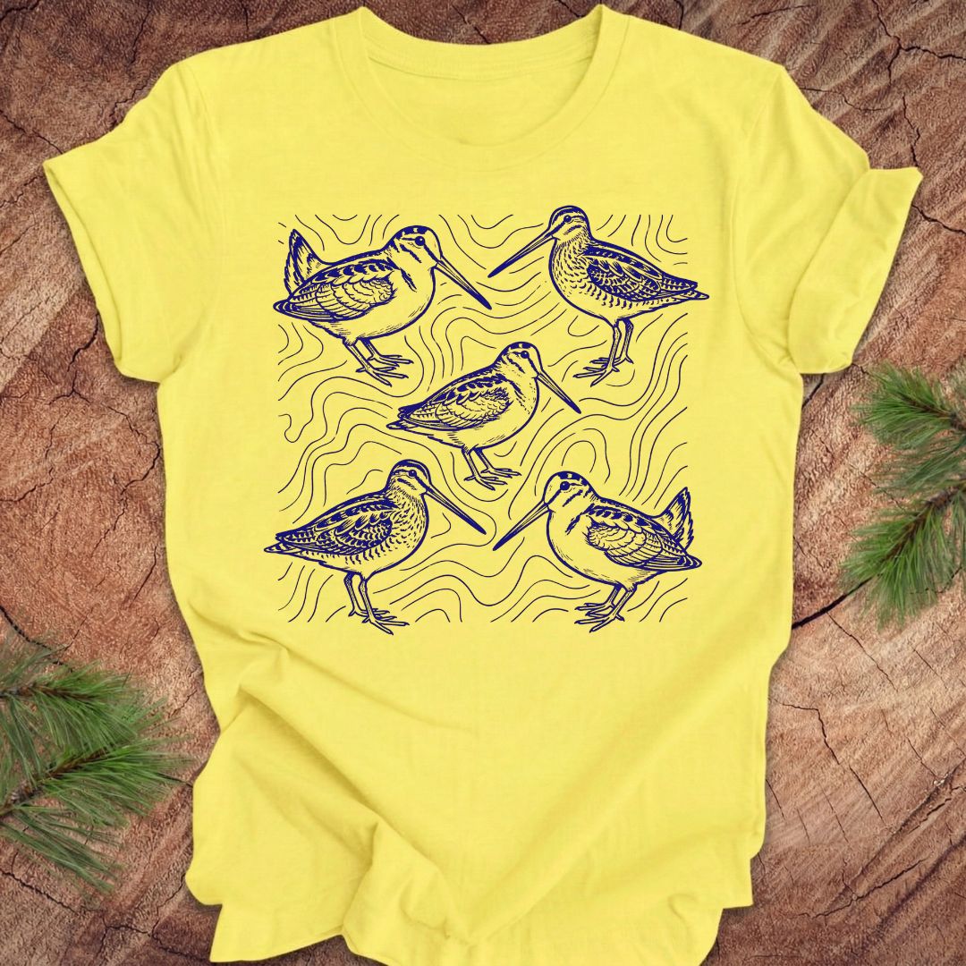Yellow t-shirt with blue woodcock and wilson's snipe bird illustrations on a wooden surface
