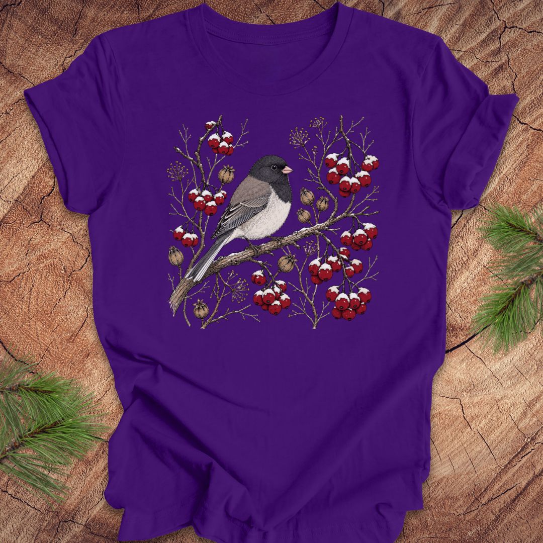 Purple t-shirt with a dark eyed junco bird and berry design on a wooden surface
