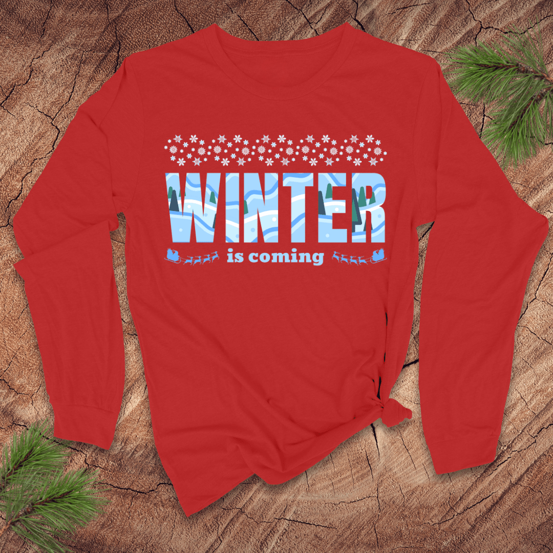 Red long-sleeve shirt with 'Winter is coming' text on a wooden surface with pine branches.