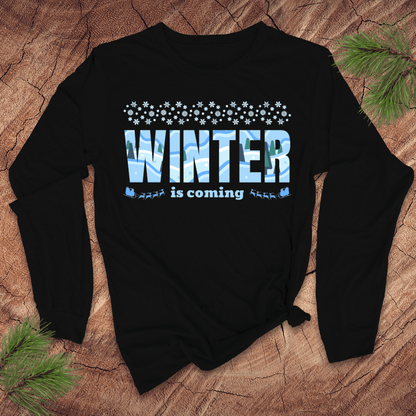 Black sweatshirt with 'Winter is coming' text on a wooden surface with pine branches.