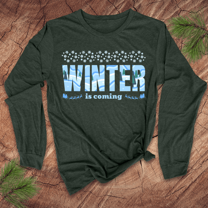 Green long-sleeve shirt with 'Winter is coming' text on a wooden surface with pine branches.