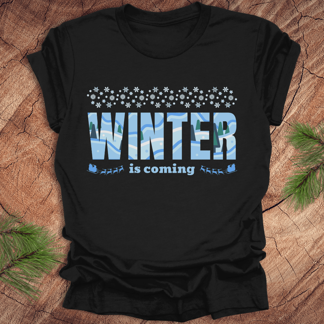 Black t-shirt with 'Winter is coming' text on a wooden surface with pine branches.
