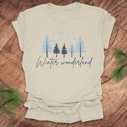 Beige t-shirt with 'Winter wonderland' text and trees with snow design on a wooden surface