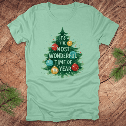 Mint green t-shirt with Christmas tree design and text on a wooden surface.