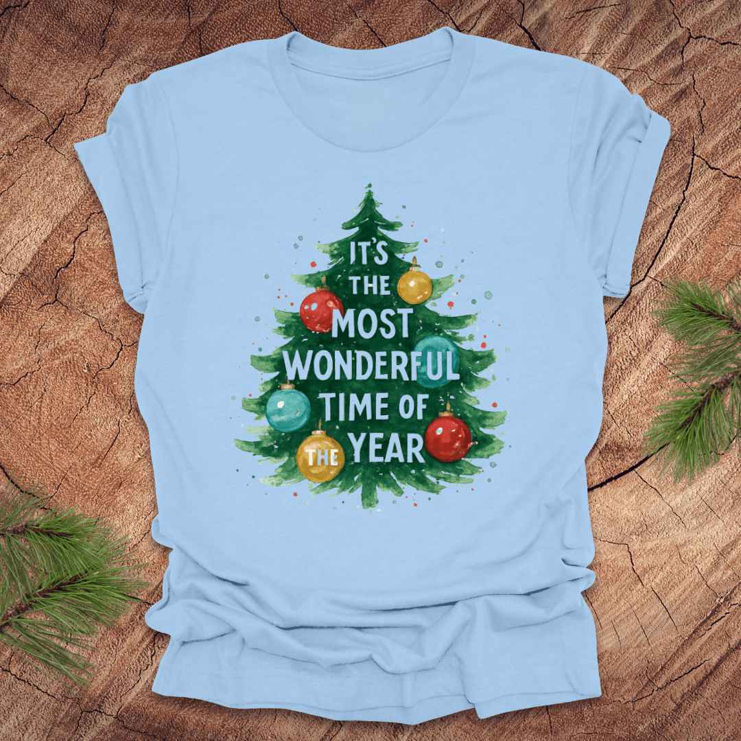 Light blue t-shirt with Christmas tree design and text on a wooden surface.