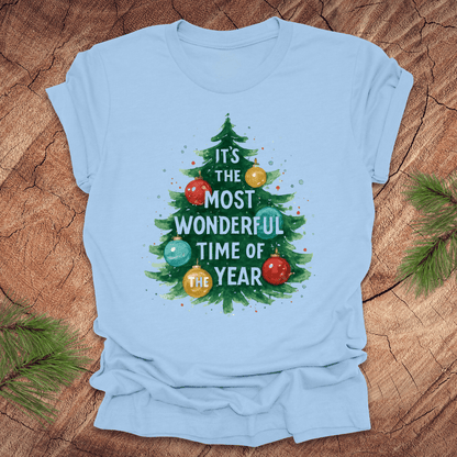 Light blue t-shirt with Christmas tree design and text on a wooden surface.