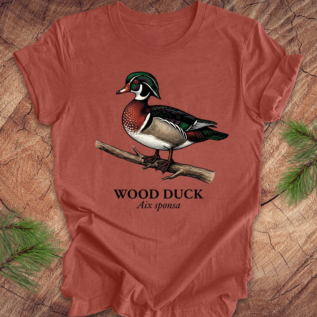Clay colored t-shirt with a wood duck graphic and text on a wooden surface.