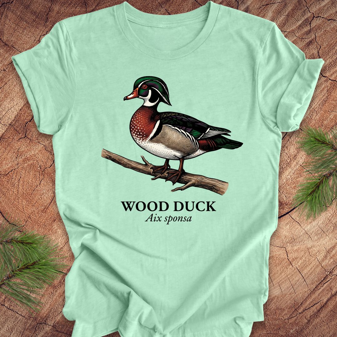 Mint green t-shirt with a wood duck graphic and text on a wooden surface.