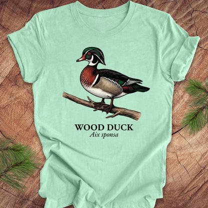 Mint green t-shirt with a wood duck graphic and text on a wooden surface.