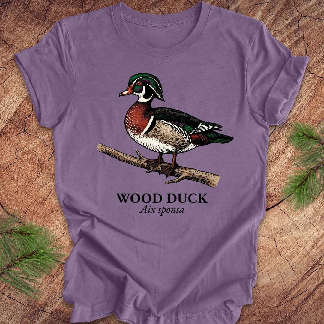 Purple t-shirt with a wood duck graphic and text on a wooden surface.