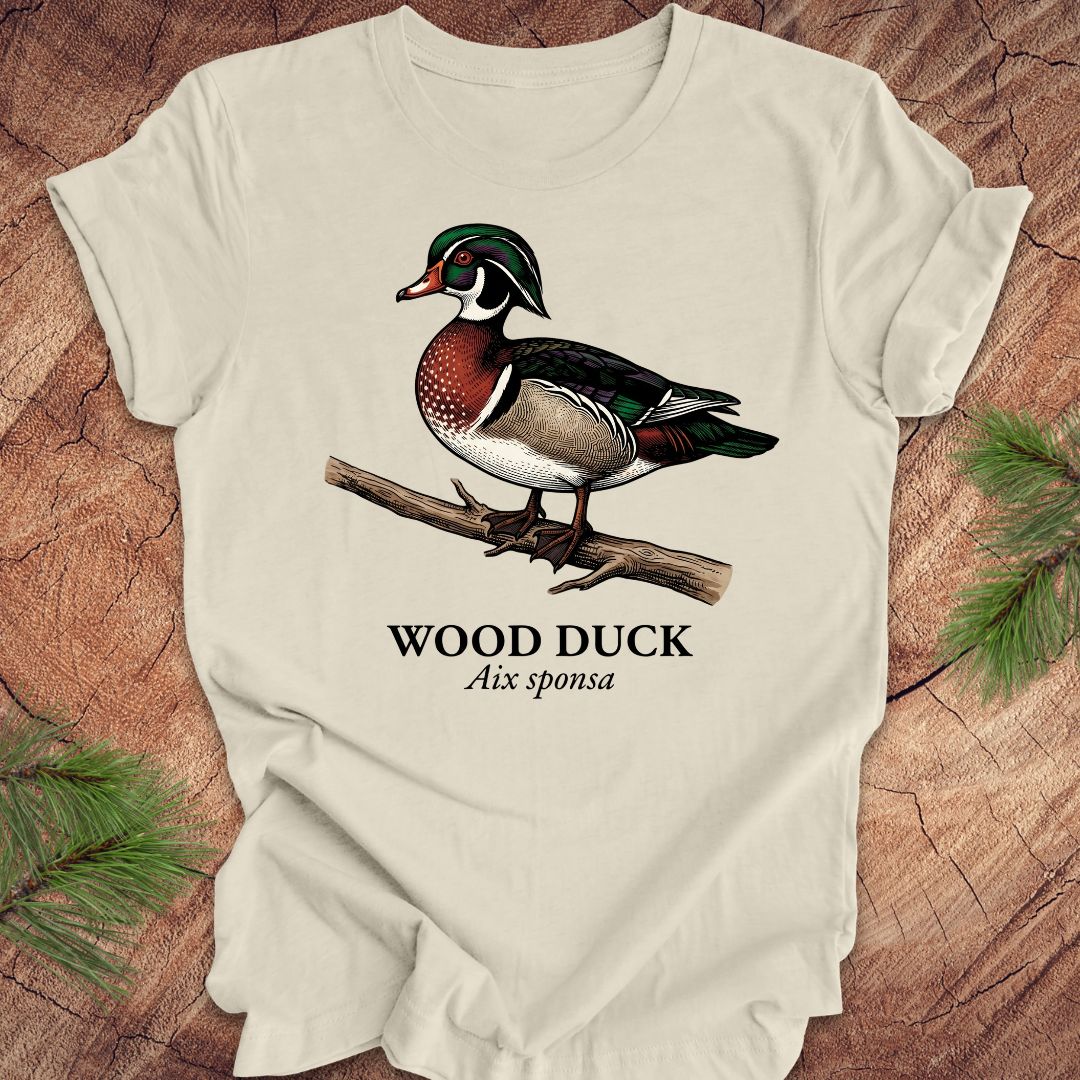 Beige t-shirt with a wood duck graphic and text on a wooden surface.