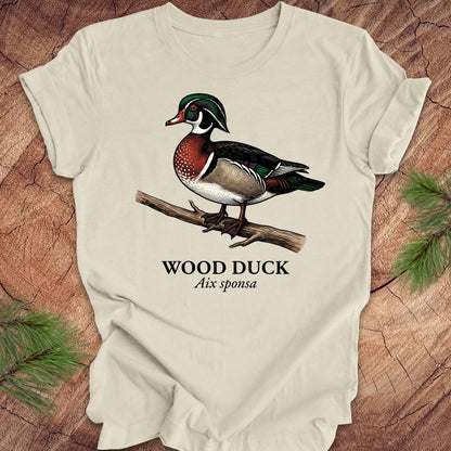 Beige t-shirt with a wood duck graphic and text on a wooden surface.